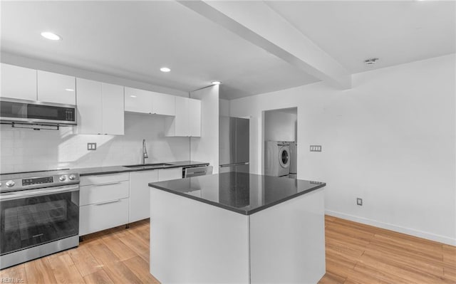 kitchen featuring sink, a center island, appliances with stainless steel finishes, washer and clothes dryer, and white cabinets