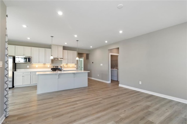 kitchen featuring pendant lighting, stainless steel appliances, a kitchen island with sink, and white cabinets