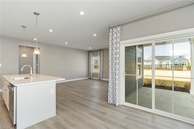 kitchen with decorative light fixtures, dishwasher, sink, a kitchen island with sink, and light hardwood / wood-style flooring