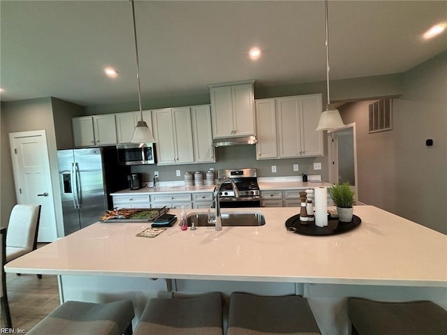 kitchen with an island with sink, appliances with stainless steel finishes, sink, and pendant lighting