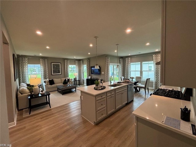 kitchen featuring sink, hanging light fixtures, wood-type flooring, a center island with sink, and stainless steel dishwasher