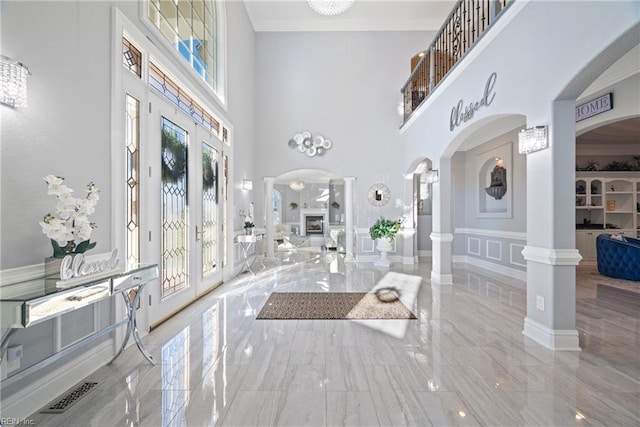 foyer entrance with french doors, a towering ceiling, ornamental molding, and ornate columns