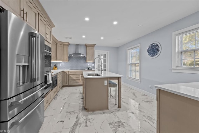 kitchen with sink, a breakfast bar area, appliances with stainless steel finishes, a kitchen island with sink, and wall chimney range hood