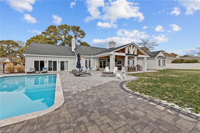 rear view of property featuring a fenced in pool, a lawn, a patio area, and an outdoor fire pit