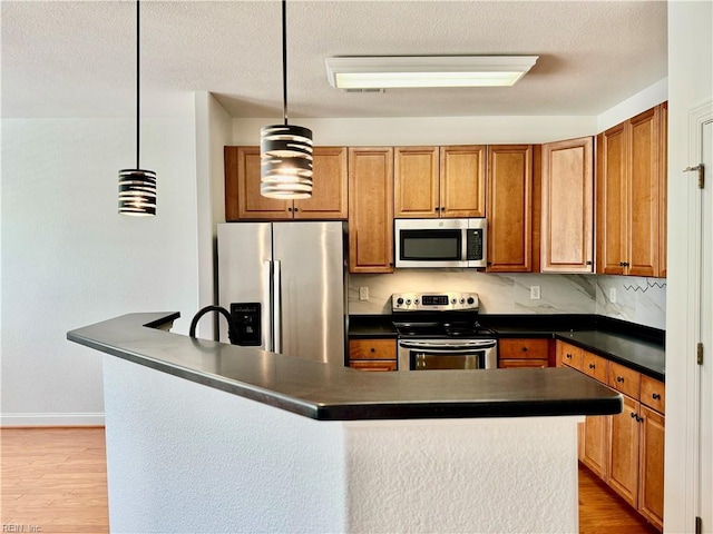 kitchen featuring a textured ceiling, hanging light fixtures, light hardwood / wood-style flooring, stainless steel appliances, and decorative backsplash