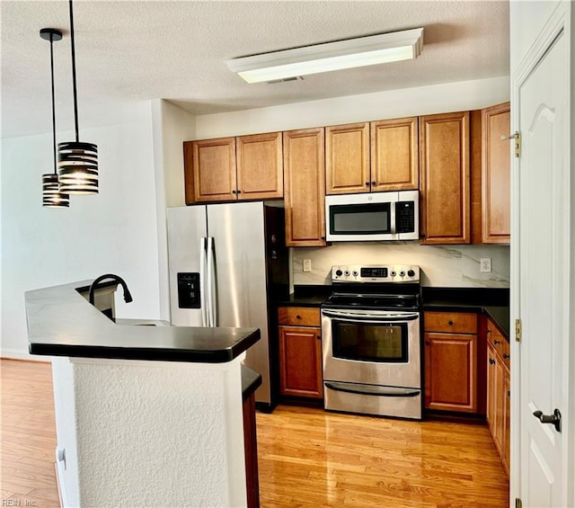 kitchen featuring appliances with stainless steel finishes, pendant lighting, a textured ceiling, and light hardwood / wood-style flooring