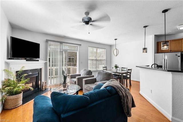 living room with ceiling fan, a high end fireplace, light hardwood / wood-style flooring, and a textured ceiling