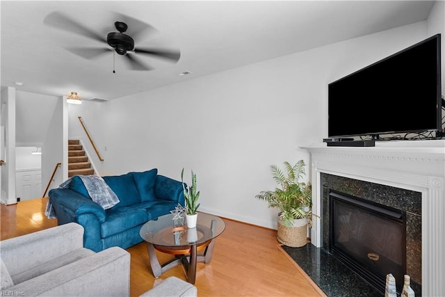 living room featuring light hardwood / wood-style flooring, a premium fireplace, and ceiling fan