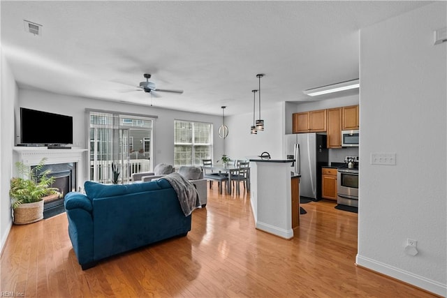 living room featuring ceiling fan, a fireplace, and light hardwood / wood-style flooring