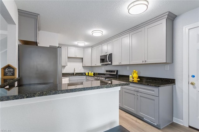 kitchen featuring stainless steel appliances, dark stone countertops, light hardwood / wood-style floors, and kitchen peninsula