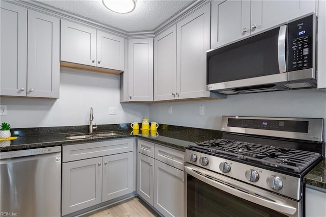 kitchen featuring sink, a textured ceiling, dark stone counters, gray cabinets, and stainless steel appliances