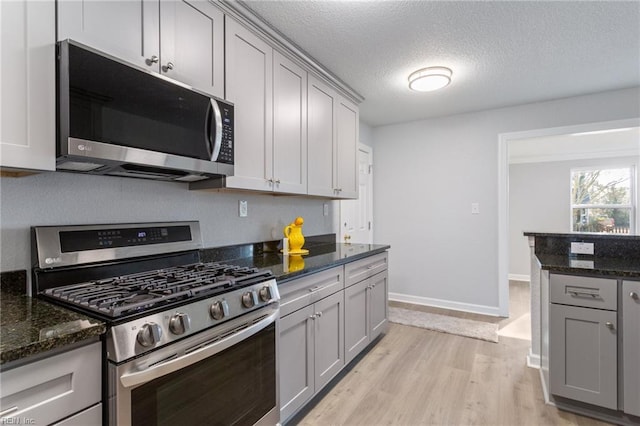 kitchen featuring gray cabinets, stainless steel appliances, light hardwood / wood-style floors, a textured ceiling, and dark stone counters