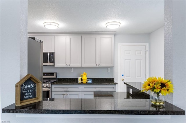 kitchen featuring white cabinetry, appliances with stainless steel finishes, a textured ceiling, and dark stone counters