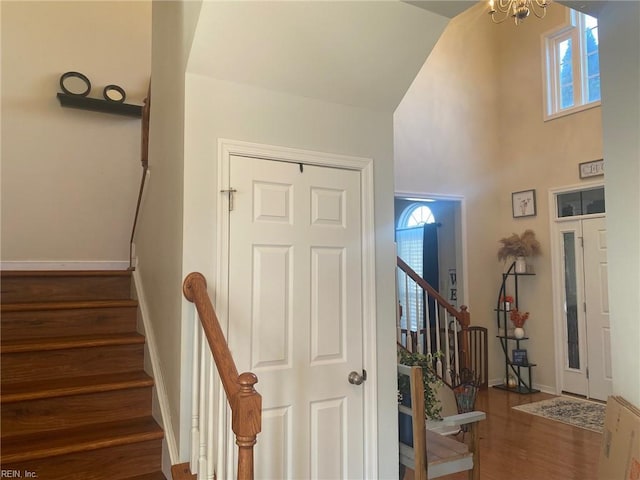 stairway with hardwood / wood-style flooring, a towering ceiling, a healthy amount of sunlight, and a chandelier