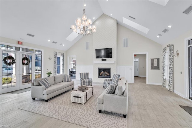 living room with high vaulted ceiling, light wood-type flooring, a fireplace, and a skylight