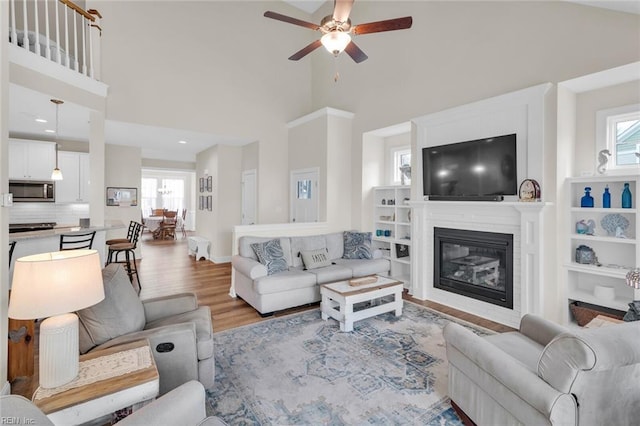 living room with light wood-type flooring, ceiling fan, and a high ceiling