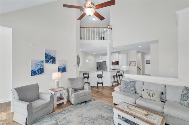 living room with ceiling fan, light hardwood / wood-style floors, and high vaulted ceiling