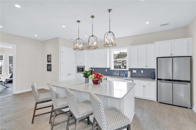 kitchen with sink, a kitchen island, pendant lighting, stainless steel appliances, and white cabinets