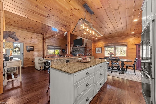 kitchen featuring wood ceiling, a center island, hanging light fixtures, light stone countertops, and white cabinets