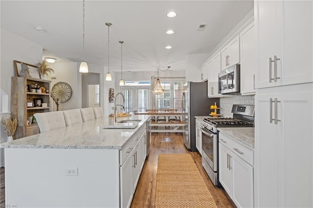 kitchen featuring a large island, sink, appliances with stainless steel finishes, hanging light fixtures, and white cabinets