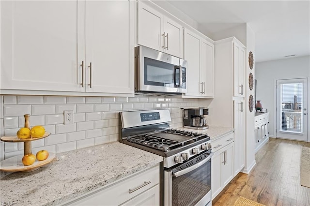 kitchen featuring backsplash, white cabinets, stainless steel appliances, light stone countertops, and light wood-type flooring