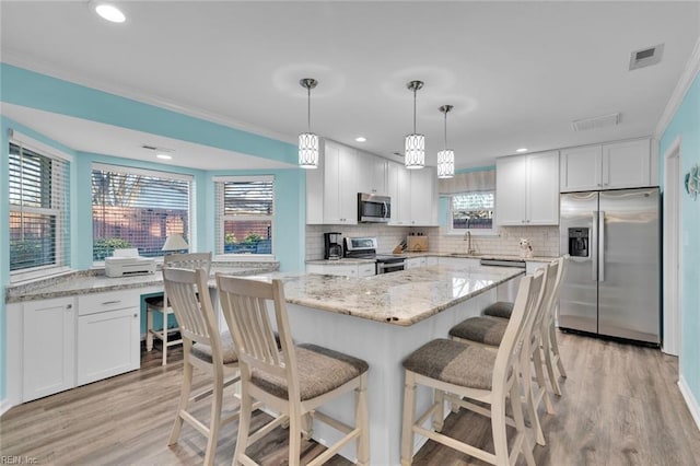 kitchen with appliances with stainless steel finishes, a center island, hanging light fixtures, and white cabinets