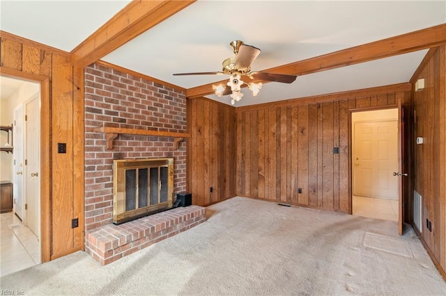 unfurnished living room featuring a brick fireplace, light colored carpet, beam ceiling, and wood walls