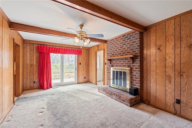 unfurnished living room featuring ceiling fan, wooden walls, a brick fireplace, light colored carpet, and beamed ceiling