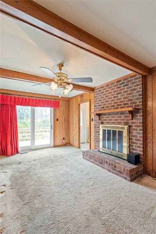 unfurnished living room with ceiling fan, beam ceiling, carpet, a fireplace, and wood walls