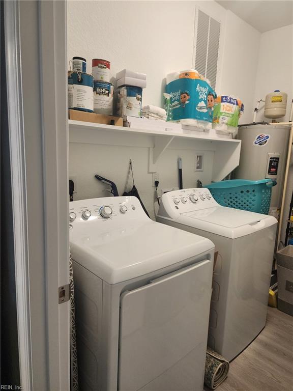 clothes washing area featuring wood-type flooring, electric water heater, and washing machine and clothes dryer