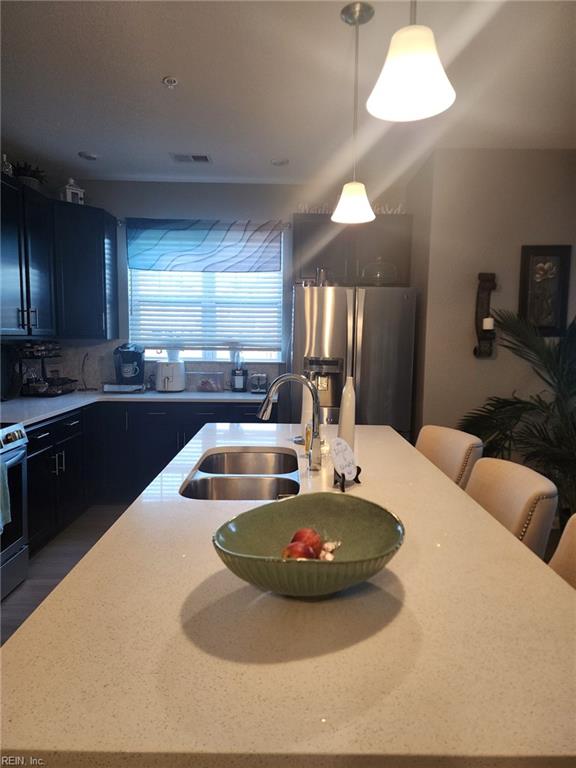 kitchen featuring appliances with stainless steel finishes, decorative light fixtures, sink, decorative backsplash, and a center island with sink