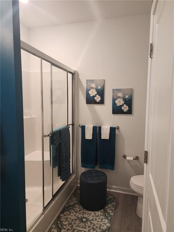 bathroom featuring hardwood / wood-style floors, a shower with shower door, and toilet