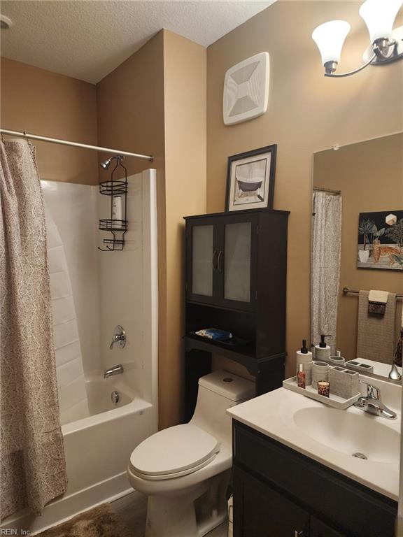 full bathroom featuring a chandelier, vanity, toilet, a textured ceiling, and shower / bath combo with shower curtain