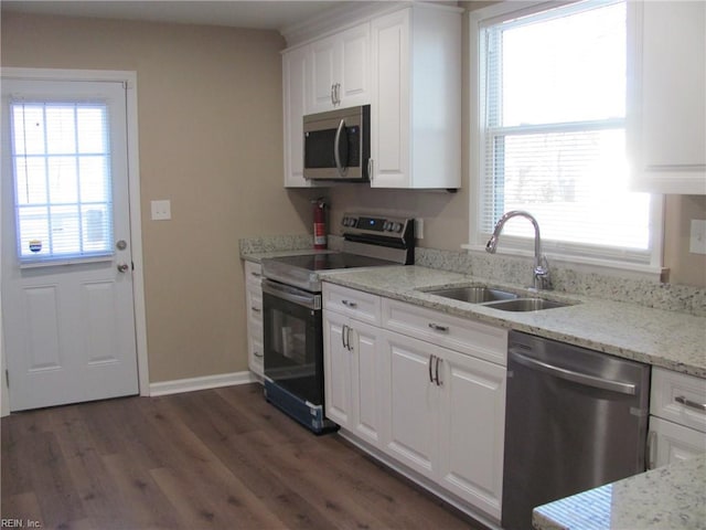 kitchen with appliances with stainless steel finishes, white cabinetry, sink, light stone countertops, and dark wood-type flooring