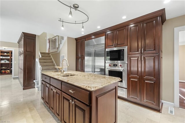 kitchen with sink, light tile patterned floors, a center island, built in appliances, and light stone counters