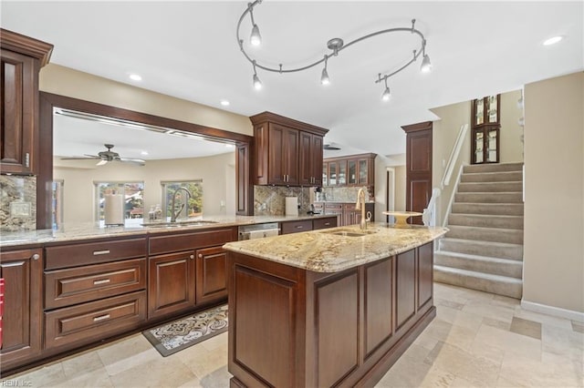 kitchen featuring an island with sink, tasteful backsplash, light stone counters, and a sink