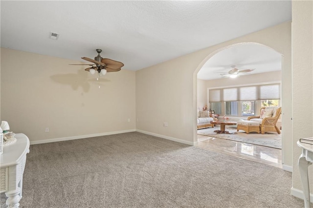 carpeted empty room featuring ceiling fan, baseboards, visible vents, and arched walkways