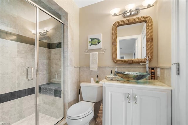 full bath featuring a stall shower, wainscoting, toilet, vanity, and tile walls