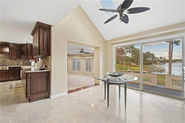 kitchen with a water view, dark brown cabinetry, high vaulted ceiling, and tasteful backsplash