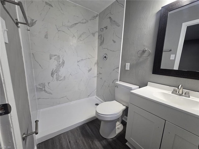 bathroom featuring vanity, wood-type flooring, toilet, and tiled shower