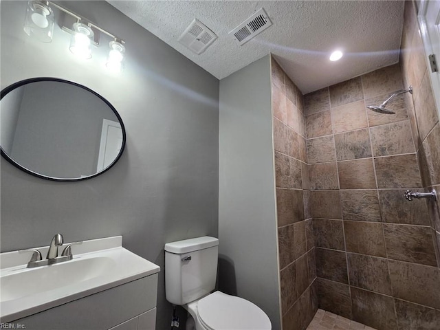 bathroom with a tile shower, vanity, toilet, and a textured ceiling