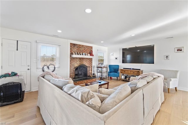 living room with a brick fireplace, a healthy amount of sunlight, and light hardwood / wood-style floors