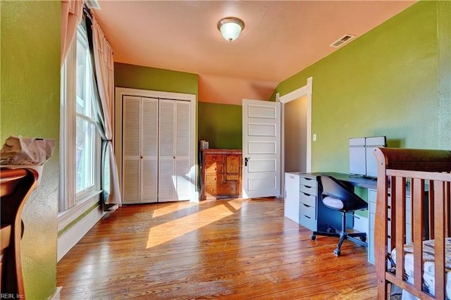 bedroom featuring vaulted ceiling, light hardwood / wood-style floors, a closet, and a nursery area