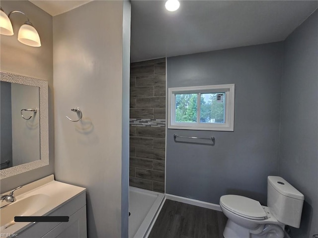 bathroom featuring a tile shower, vanity, hardwood / wood-style floors, and toilet