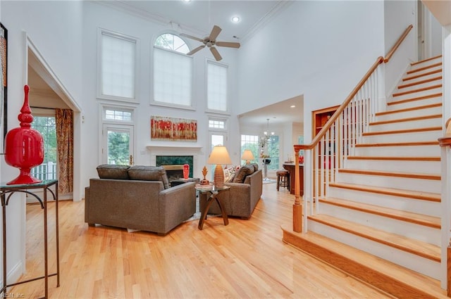 living room with a premium fireplace, ornamental molding, a towering ceiling, and light wood-type flooring