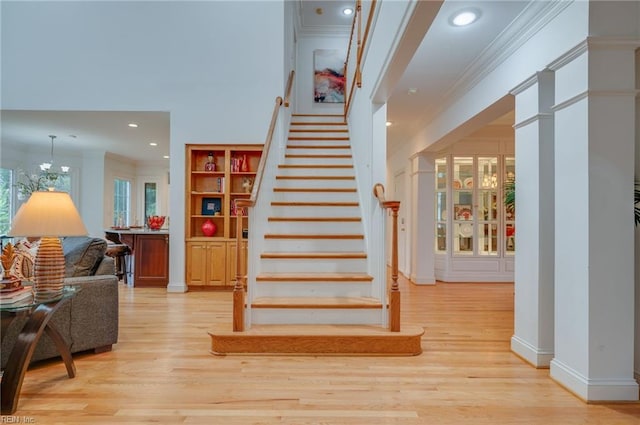 stairs with ornamental molding, wood-type flooring, a chandelier, and built in features