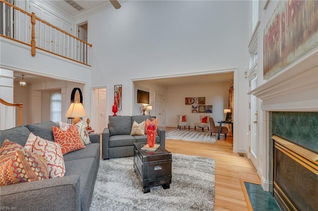 living room with hardwood / wood-style flooring, a tile fireplace, a high ceiling, and crown molding