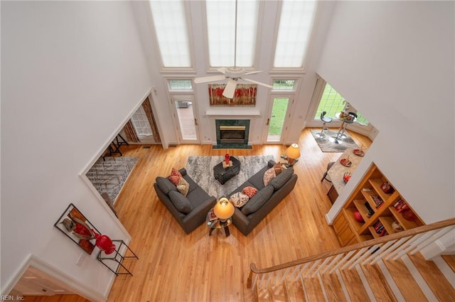 living room featuring ceiling fan, wood-type flooring, a fireplace, and a high ceiling