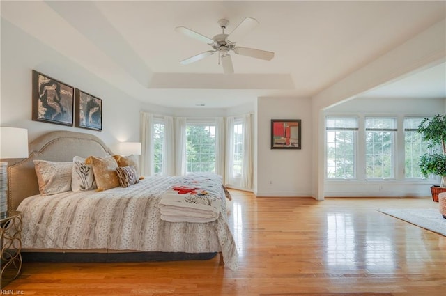 bedroom with a raised ceiling, multiple windows, ceiling fan, and light hardwood / wood-style flooring