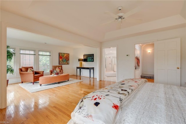 bedroom featuring ceiling fan, ensuite bath, a raised ceiling, and light hardwood / wood-style floors